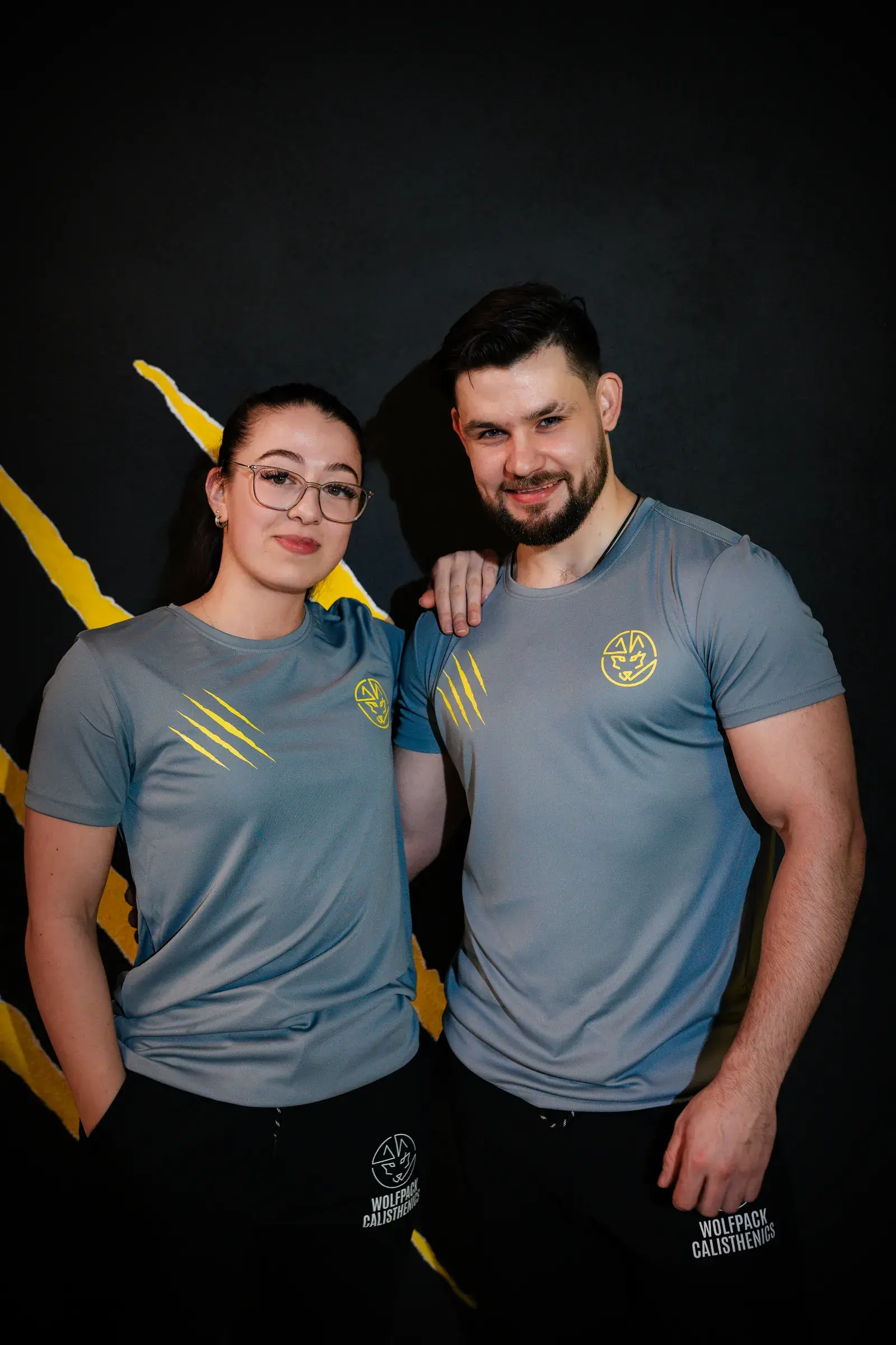 Twee lachende mensen in een Wolfpack-shirt voor de muur met de gele klauw in de gym in Berchem