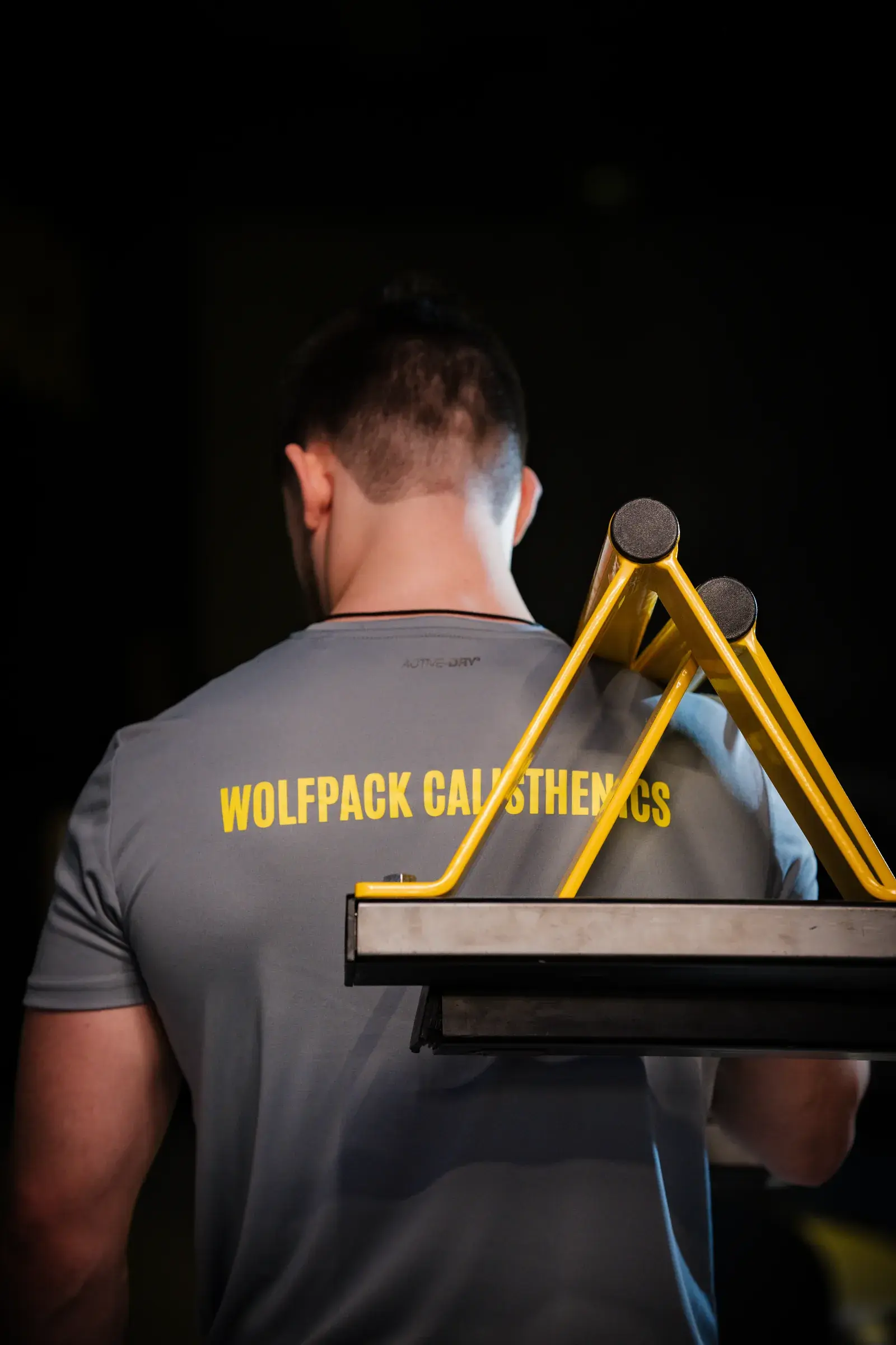 Athlete in a grey Wolfpack shirt with a yellow back print, in front of yellow parallettes