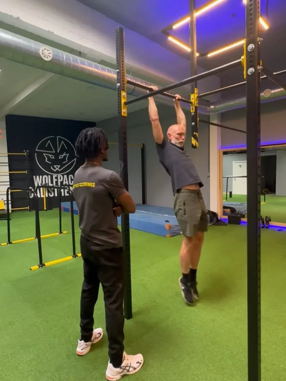 Een coach begeleidt een sporter bij de pull-upstang